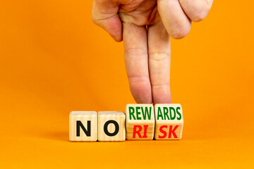 No risk or rewards symbol. Businessman turns wooden cubes and changes words 'no risk' to 'no rewards'. Beautiful orange background. No risk or rewards and business concept. Copy space.