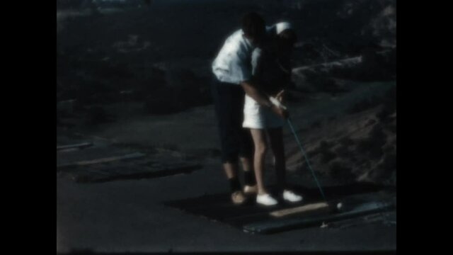 Swing Practice 1959 - A teen boy helps his girl friend with her golf swing at a driving range at a southern California golf course, 1959. 