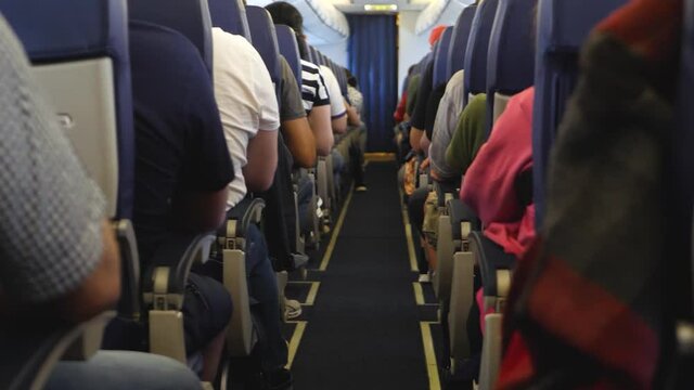 Unrecognizable passengers on seats in interior of airplane. View inside in plane. Long and boring fly. Economy lowcost flight in cabin. No social distance