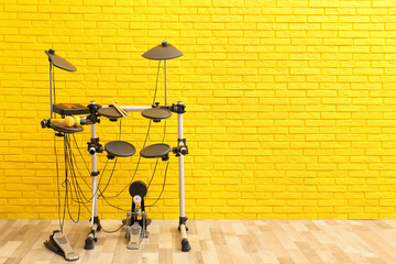 Modern electronic drum kit near yellow brick wall indoors, space for text. Musical instrument