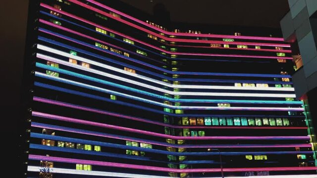Multicolored illumination on a tall building. Rapidly changing color lines. Large office building in the city center