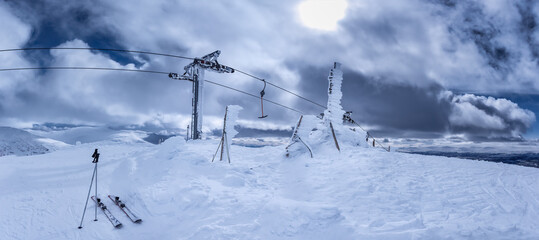Scenic panorama of frozen under strong cold wind snow and ski lift at mountain top, one par of ski...