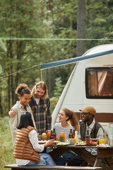 Vertical shot of diverse group of friends enjoying picnic outdoors at campsite with trailer van - obrazy, fototapety, plakaty