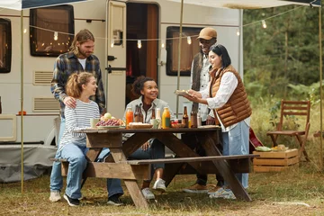 Foto op Plexiglas Kamperen Volledig zicht op diverse groep jonge mensen die buiten genieten van een picknick tijdens het kamperen met een aanhangwagen