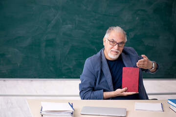 Old male teacher holding book in the classroom