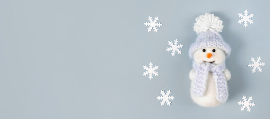 Christmas banner with white snowflakes and a cute snowman on a pastel blue background. Copy space, top view, flat lay.