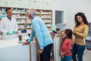 Professional pharmacist talking with customers in modern drugstore.
