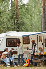 Vertical full length portrait of friends enjoying outdoors while camping with van in forest, copy...