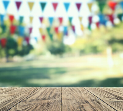 Empty wooden table in park decorated with bunting flags, space for design. Outdoor party