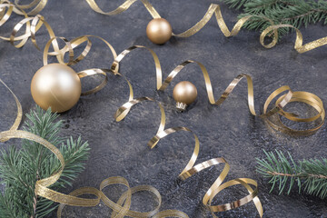 Christmas composition of yellow Christmas balls, fir branches and a gold ribbon on a black with gold embossed background.
