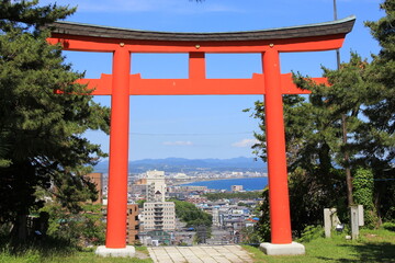 朱塗りの明神鳥居越しに、海沿いの街がある風景