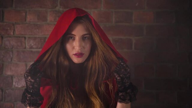 Beautiful young woman with long hair, red lips in red cloak and hood