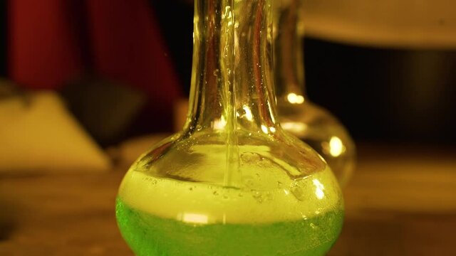 Two bottles of green liquid are on wooden table. Glass vials with potion