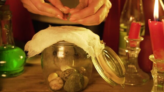 Witch prepares green potion in jar on wooden table at night. Preparing for halloween. Fortune teller