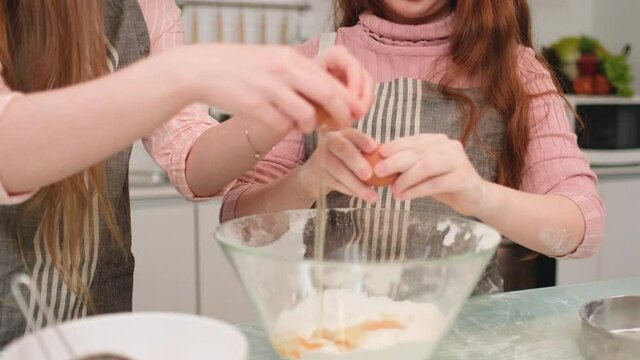 Close up hands of mother and daughter crack an egg to put into bowl with flour during making cake by mix all ingredients together.