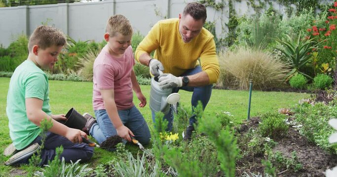 Happy caucasian father with two sons gardening together and watering plants in garden