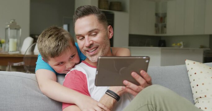 Happy caucasian father with son sitting in living room and using tablet