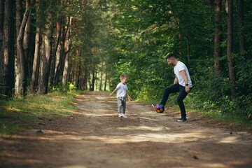 Fototapeta premium man with little son playing football together digging ball in forest spend time together having fun weekend