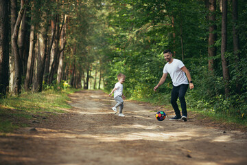 man with little son playing football together digging ball in forest spend time together having fun...