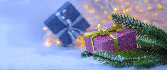 Beautiful Christmas gifts of pink and silver color with a gold ribbon on blue snow and fir branches against a background of beautiful bokeh.