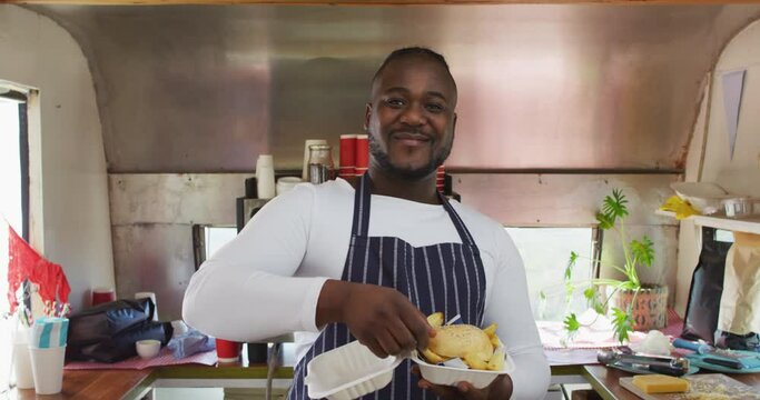 Smiling african american male business owner holding takeaway meal in food truck