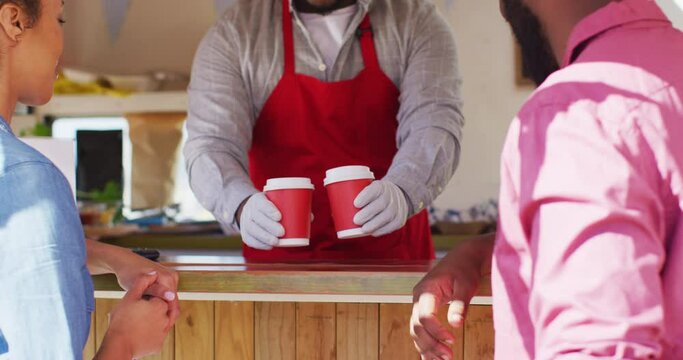 Male food truck owner wearing gloves serving coffees to happy couple and making thumbs up sign