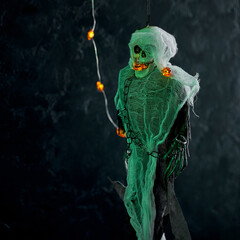 Halloween decoration a skeleton in a white cape decorated with a garland of glowing pumpkins