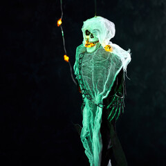 Halloween decoration a skeleton in a white cape decorated with a garland of glowing pumpkins