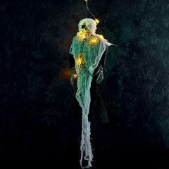 Halloween decoration a skeleton in a white cape decorated with a garland of glowing pumpkins