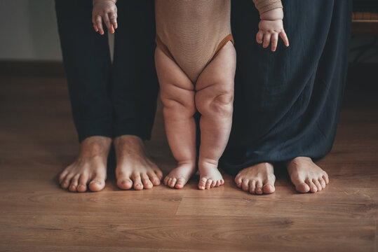 young married couple are standing together with a small child on the wooden floor in the room with bare feet close-up