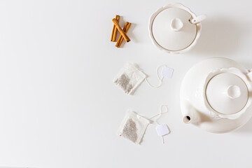 Composition with cup of tea, teapot, sugar pot, cinnamon and tea bag on white background. Flat lay, top view. Slow morning concept.