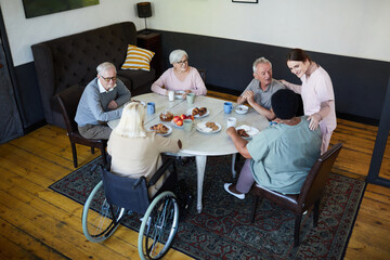 High angle view at diverse group of senior people enjoying breakfast at dining table in nursing home, copy space