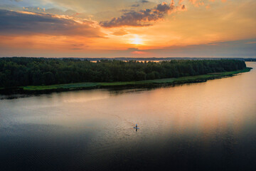 Fototapeta premium Man with stand up paddleboard in water during sunrise