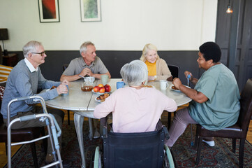 Diverse group of senior people chatting at dinner table in nursing home