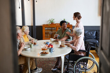 Through door view at diverse group of senior people enjoying breakfast in cozy nursing home