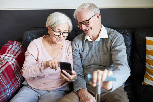 High angle portrait of smiling senior couple using smartphone in nursing home, copy space