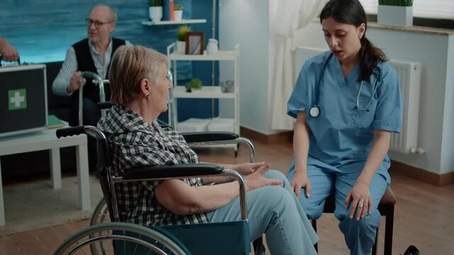 Disabled senior woman in nursing home talking to nurse for healthcare examination and checkup. Medical assistant giving advice for recovery to elder patient with handicap in wheelchair.