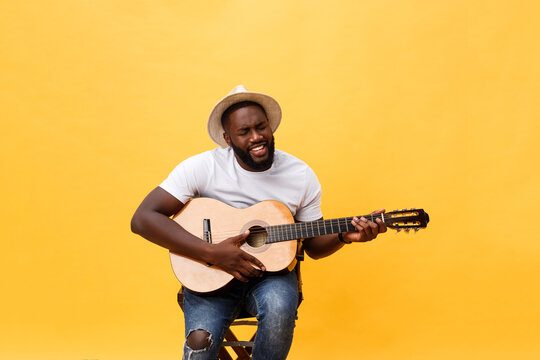 Handsome African American Retro Styled Guitarist Playing Acoustic Guitar Isolated On Yellow Background.