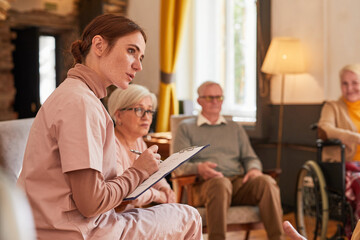 Portrait of young woman talking to group of senior people during therapy session at retirement home, copy space