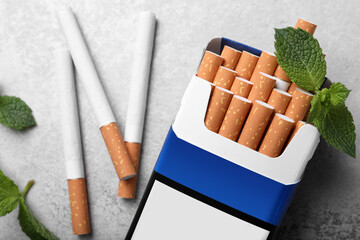 Pack of menthol cigarettes and mint leaves on grey table, flat lay