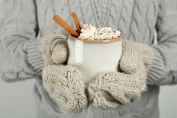 Woman in knitted mittens holding cup of delicious hot chocolate with marshmallows and cinnamon sticks, closeup