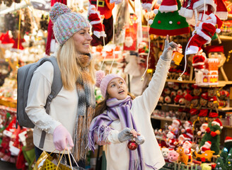 Happy daughter with mom point finger at selected christmas tree decorations at street christmas market