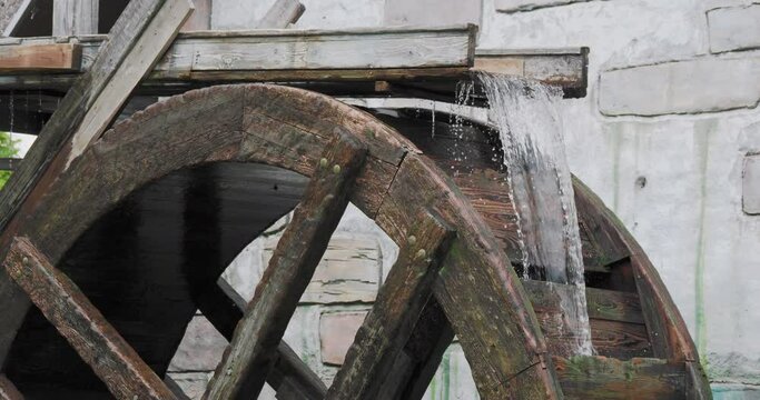 Stream of flowing water turns the wooden wheel of an old water mill.