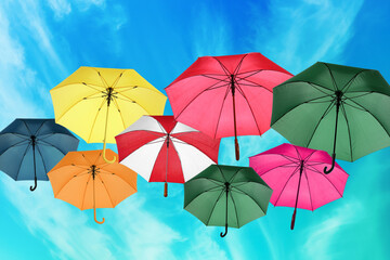 Group of different colorful umbrellas against blue sky with white clouds on sunny day