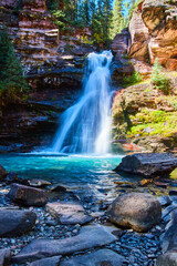 Beautiful waterfall with blue water and large boulders at bottom of canyon