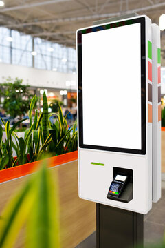 Self-service electronic counter with blank mockups on white screen and payment terminal in fast food restaurant, shopping mall. Side view