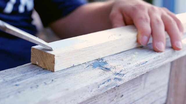 Chisel used to scrape paint off of a wooden board. Two slow motion clips of a handicapped persons hands at work.