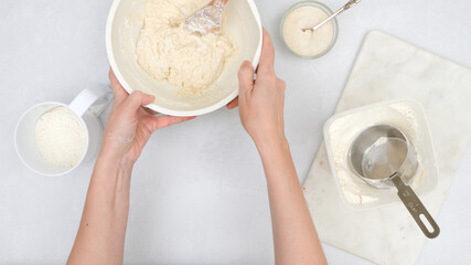 Bread dough recipe. Mixing dough in a bowl, step by step baking process, flat lay, woman hands