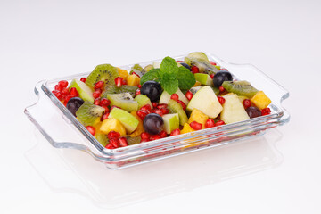 Mixed fruit salad arranged in a transparent rectangle tableware and garnished with mint leaf.