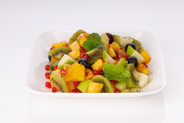Mixed fruit salad arranged in a transparent rectangle tableware and garnished with mint leaf.